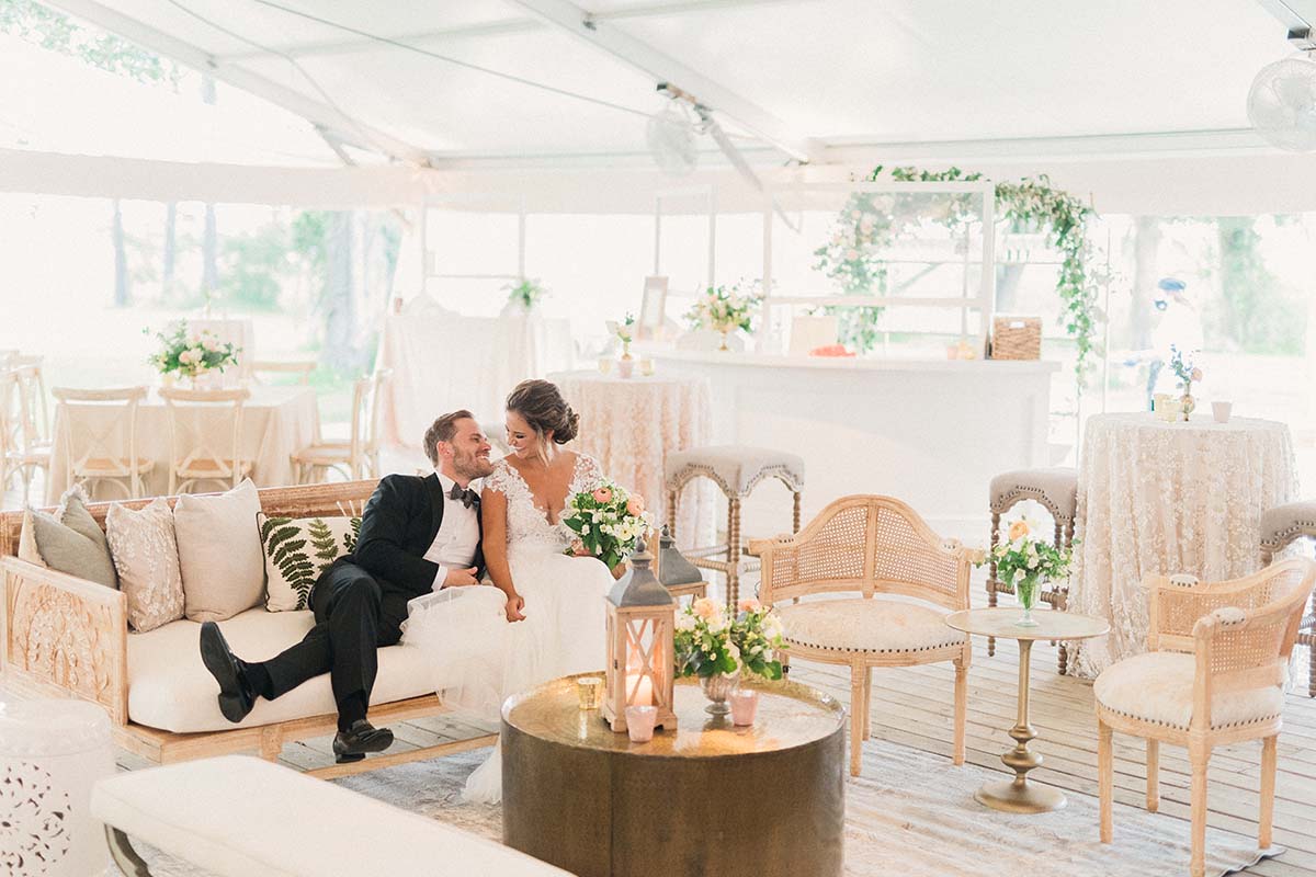 Bride and groom in reception tent decorated in neutral palette with greenery and lots of texture in fabrics